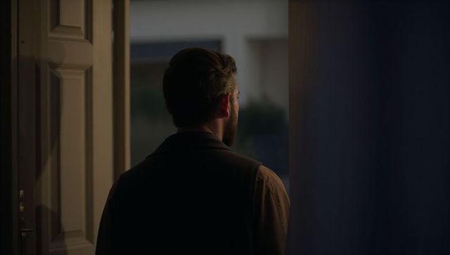 Backlit man standing at doorway gazing into dusk, cinematic silhouette at home threshold