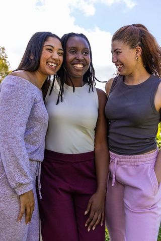 Smiling friends leaning together in sunny park wearing colorful casual attire and earrings