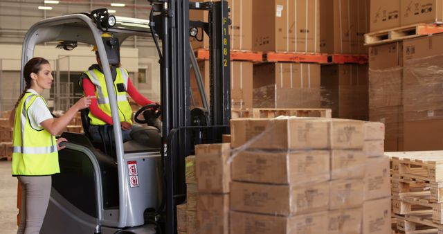 Diverse male and female colleague instructing and operating forklift truck at warehouse, copy space. Teamwork, equipment, organisation, storage, transport, shipping and industry, unaltered.