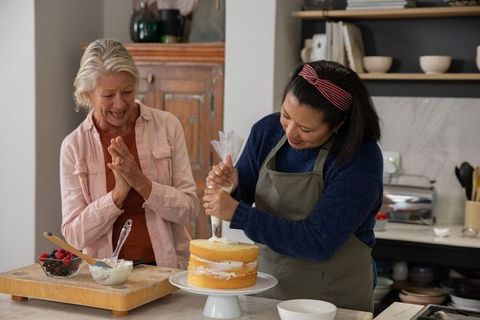 Friends decorating layer cake together in cozy kitchen, baking, smiling, sharing joy