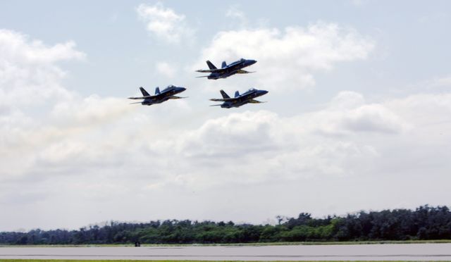 The image shows US Navy's Blue Angels F/A-18 jets flying above the runway at NASA's Kennedy Space Center. Ideal for use in promotional materials for air shows, especially military air demonstrations. This visual also works well in articles and blog posts about aviation events, military air units, and precision flying. Additionally, it can be used for educational purposes when talking about flight demonstrations and aircraft. The photo captures the precision and skill of the Blue Angels, making it a captivating addition to presentations and brochures.
