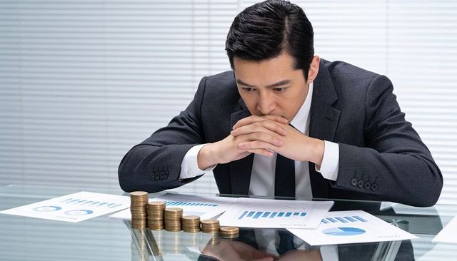 Businessman studying financial reports and coin stacks showing cash flow stress and risk