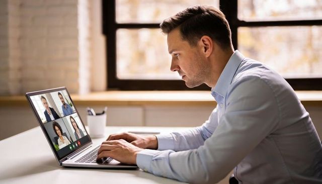 Focused young professional typing during remote video meeting in window-lit home office