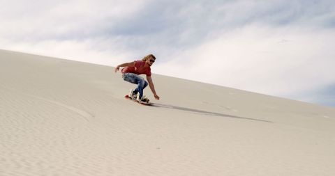 Young Man Sandboarding on Desert Dune Under Blue Sky