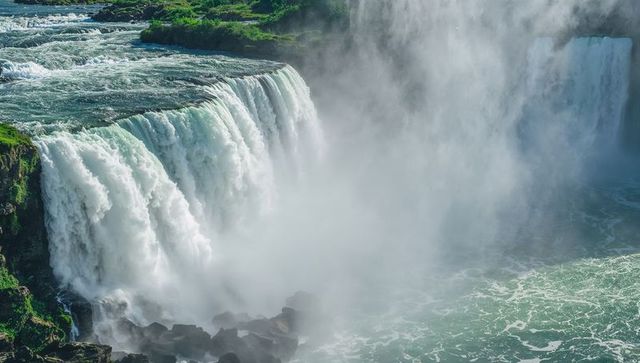 Cascading waterfall plunging over rocky cliff with emerald river mist and foam