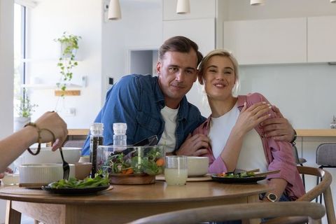 Sunlit couple sharing intimate salad meal at round wooden dining table in modern kitchen