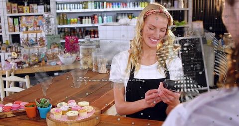 Smiling barista processing card payment at rustic bakery counter with cupcakes and succulents