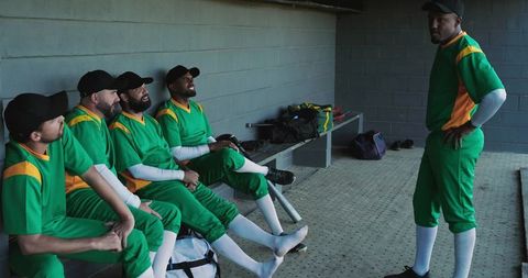 Baseball teammates relaxing in dugout wearing green uniforms preparing for game