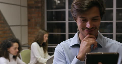 Businessman Using Tablet in Modern Office with Coworkers in Background