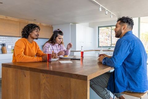 Friends chatting over casual meal at wooden kitchen island with bottled drinks