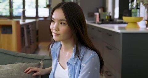 Asian Woman Relaxing on Sofa in Modern Minimalist Kitchen