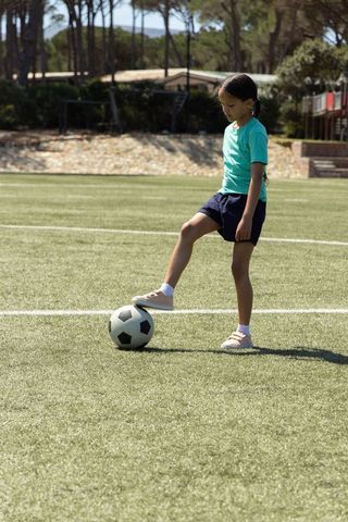 Young girl balancing on soccer ball while practicing skills on sunlit turf