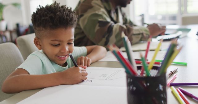 Child enjoying drawing while a military parent works in the background. Perfect for content related to family bonding, children, creativity, education, and military families. Suitable for websites, blogs, and articles focused on parenting, family activities, and the life of military families.
