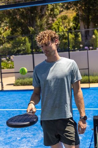 Young man practicing padel on bright blue court with black perforated racket during sunny practice