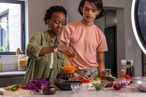 African American woman and Asian man preparing vibrant salad at kitchen island with ring light