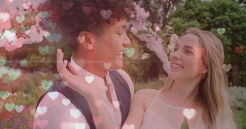 Smiling romantic couple exchanging loving gaze beneath floral arch in garden with heart bokeh