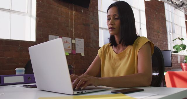 Biracial businesswoman sitting at desk using laptop looking ahead. business in a modern office.