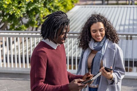 Diverse friends sharing tablet and smartphone on outdoor terrace, casual collaboration