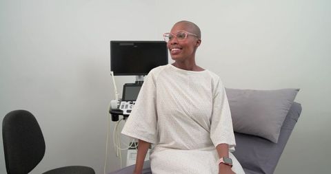 Smiling african woman sitting on clinic exam table wearing gown beside ultrasound machine