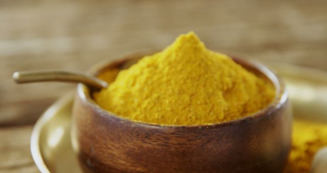 Close-up of bright yellow turmeric powder in a simple wooden bowl with a spoon resting in it. Ideal for recipes, culinary blogs, and health articles highlighting spices, cooking ingredients, and natural wellness.