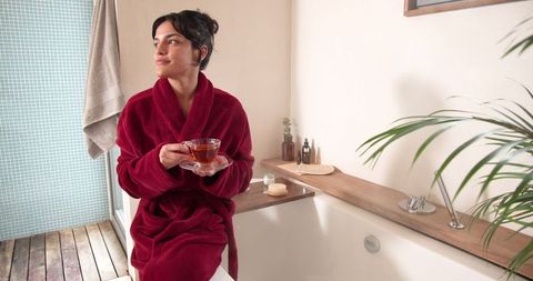 Woman in red bathrobe relaxing in modern bathroom with tea