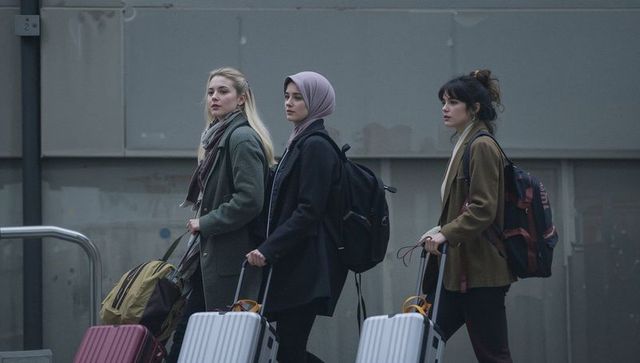 Three female travelers walking with rolling suitcases and backpacks on urban platform