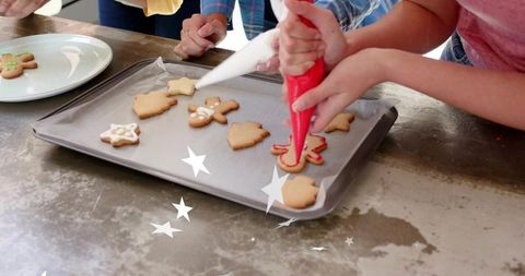 Hands decorating gingerbread cookies with colorful icing using piping bags on baking tray