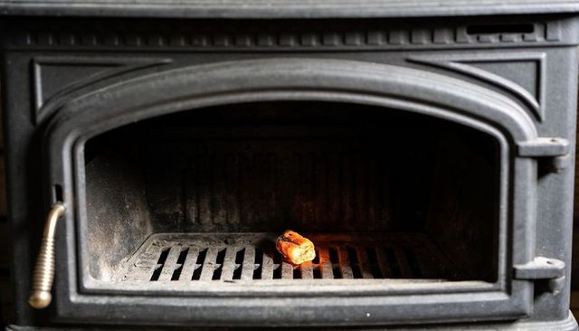 Glowing ember casting warm amber light inside cast-iron wood stove firebox, rustic hearth