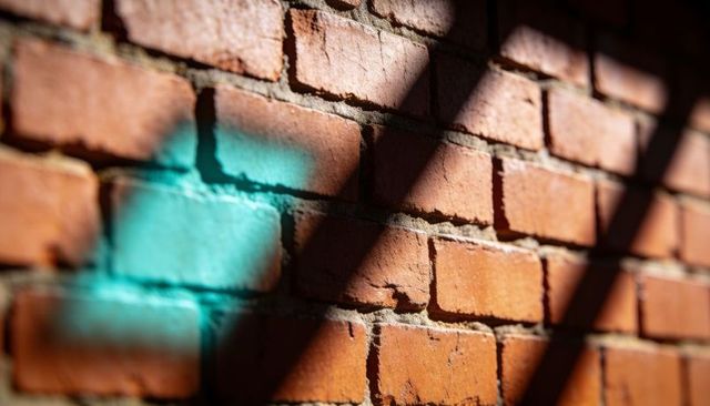 Sunlit red brick wall catching turquoise paint smear and diagonal shadows