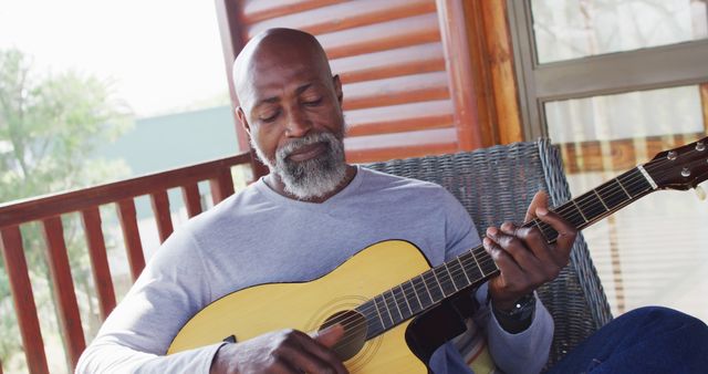 Senior african american man on balcony in log cabin playing guitar. Log cabin and lifestyle concept.