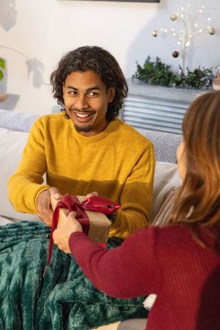 Smiling man receiving wrapped gift on cozy sofa during festive holiday evening at home