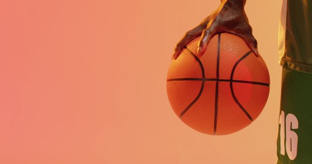 Image of midsection of african american male basketball player holding ball on orange background. Sports and competition concept.