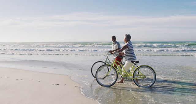 Senior couple riding bicycles along the peaceful beach shoreline with the ocean and waves in the background. The scene portrays an active and happy lifestyle during retirement. Suitable for marketing health and wellness programs, travel and adventure companies, senior living communities, and ads promoting an active lifestyle.