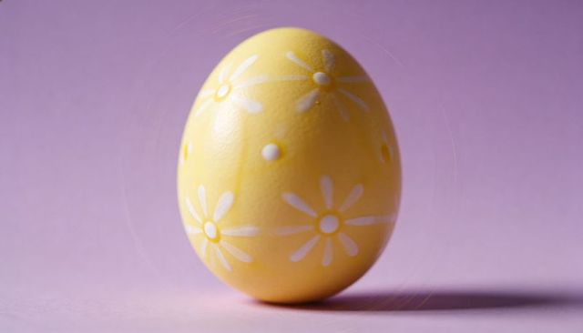 Yellow easter egg with white daisy motif on pastel pink background