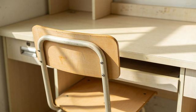 Sunlit school desk and chair catching warm morning light, scuffed wood texture, minimal study nook