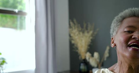 Senior african american woman laughing by window with natural light and cozy living room