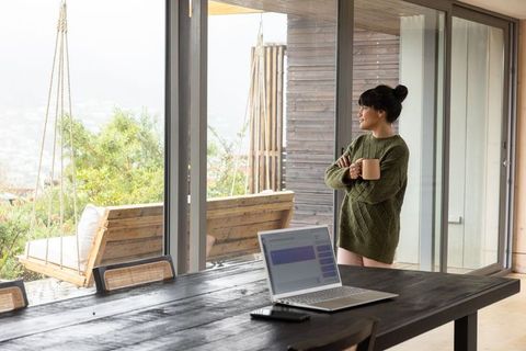 Woman Relaxes with Mug in Rustic Home by Large Windows