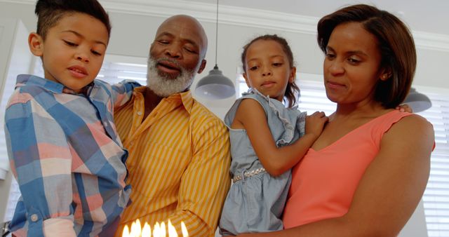 Front view of black family celebrating birthday in kitchen of comfortable home. Parents holding children and looking at birthday cake 4k