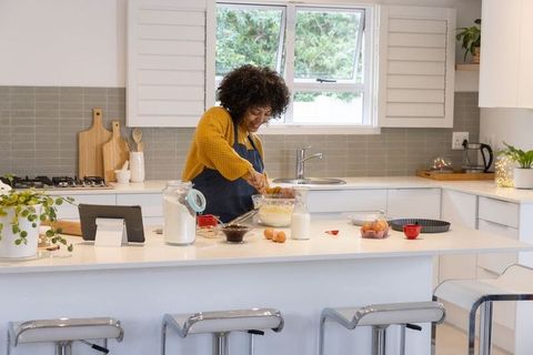 African american woman stirring batter on modern kitchen island while following tablet
