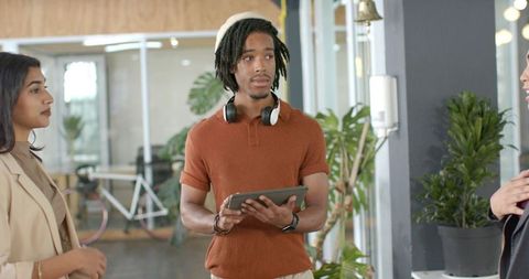 Young professional leading team discussion in coworking space with tablet and headphones