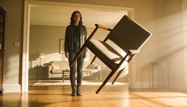 Woman standing in doorway with floating midcentury chair while sunlight streams through
