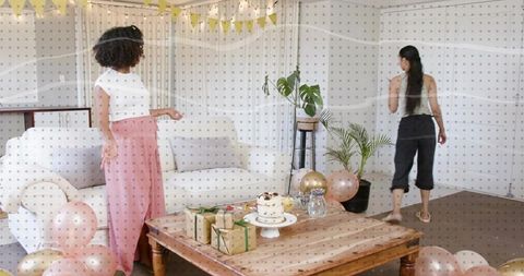 Two women celebrating casual home party in living room with cake gifts balloons bunting