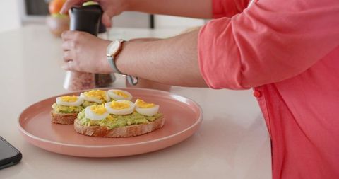Indian Woman Seasoning Avocado Toast with Egg Slices in Modern Kitchen