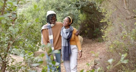 African american couple walking on forest trail wearing sweaters and scarves