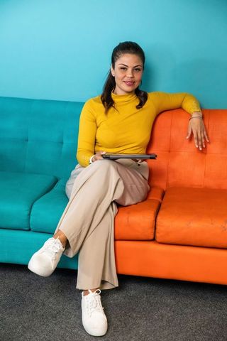 Female professional sitting on colorblock sofa holding tablet wearing white sneakers