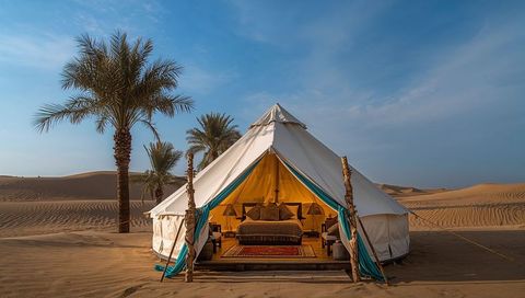 Luxury desert glamping bell tent with king bed, lantern light and palm oasis on sand dunes
