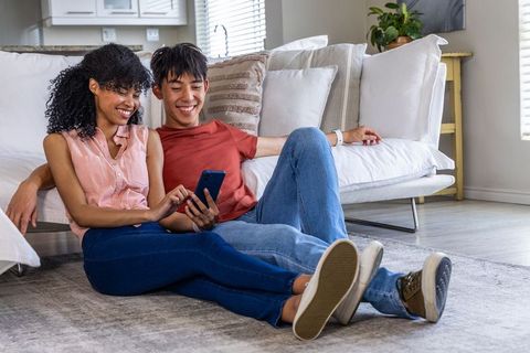 Couple sharing viral content on smartphone while relaxing on living room floor
