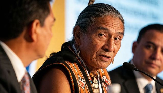 Native american elder speaking at leadership panel wearing woven vest with feather