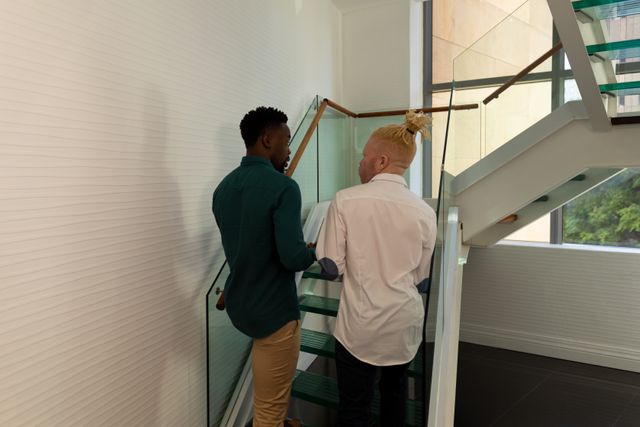 Rear view of african american mid adult businessman with albino male colleague on steps in office. unaltered, abnormal, corporate business, teamwork, occupation and office concept.