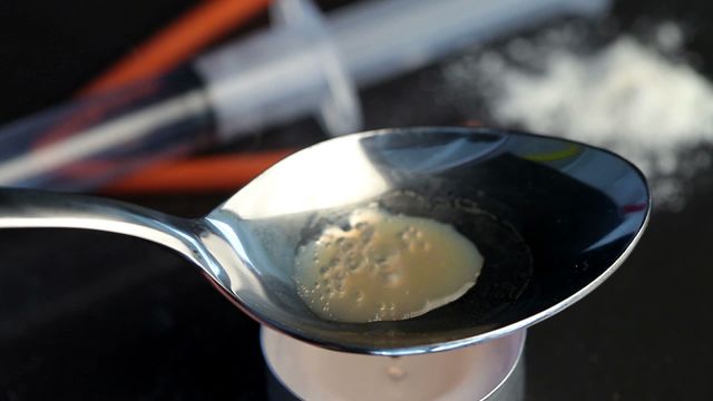 Heroin dissolving in a spoon heated by candle flame. Suitable for discussions on drug addiction, societal challenges of substance abuse, anti-drug campaigns, awareness programs, or educational presentations about drug use consequences.